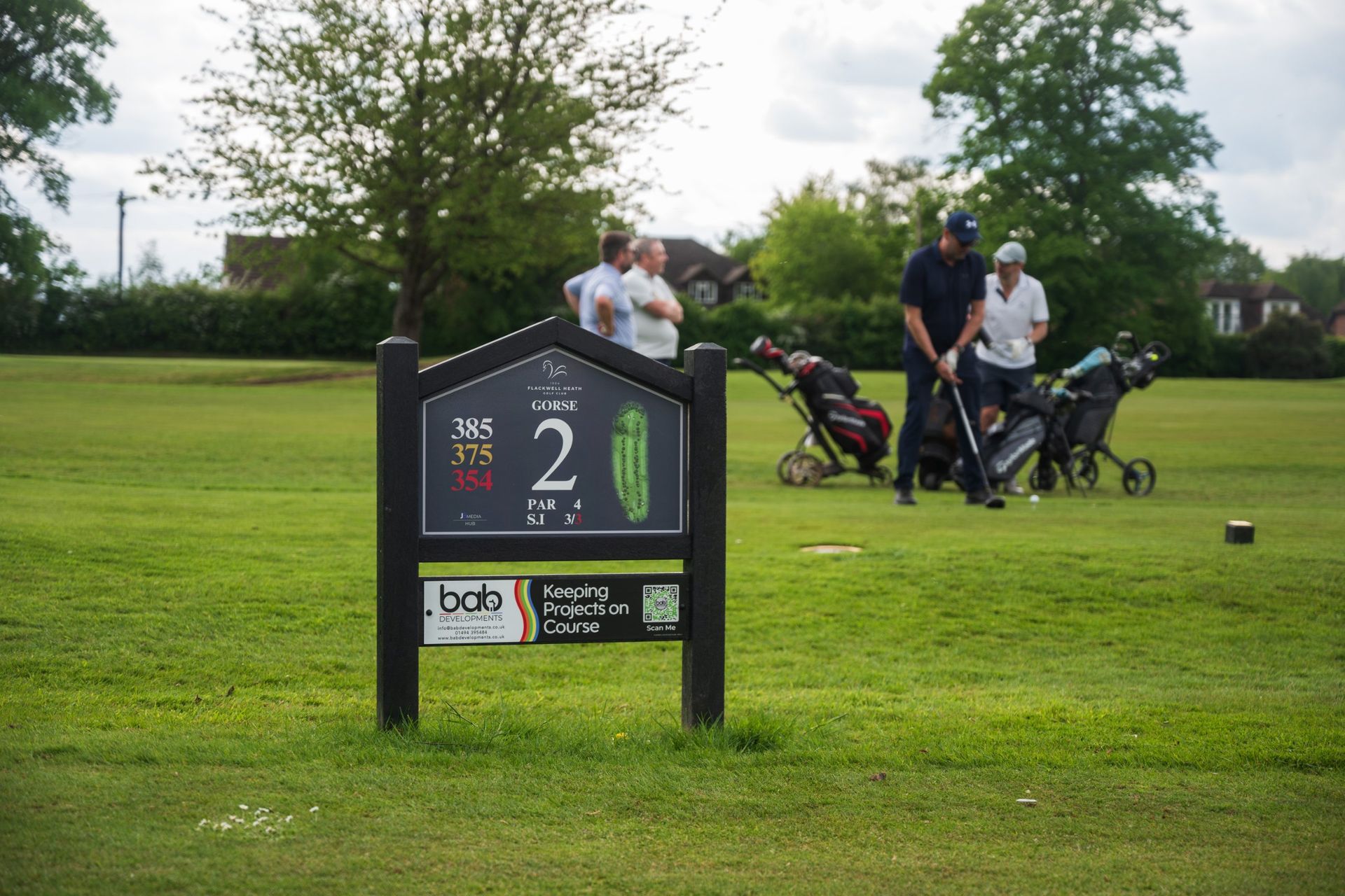 A JB Golf tee sign on the course, with golfers teeing off behind it