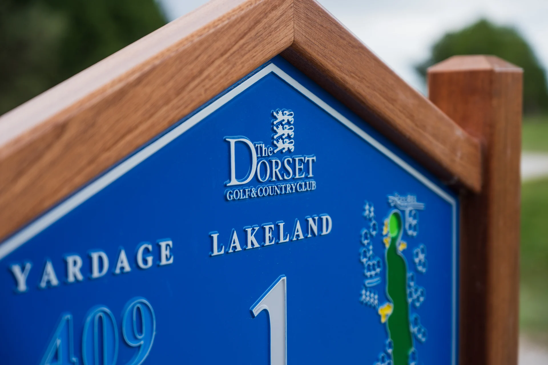 Close-up of the timber grain, blue sign face and detailed lettering at The Dorset Golf and Country Club
